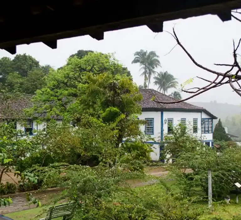 Fachada do casarão histórico da Fazenda Santa Rita em Muqui, cercado por natureza e jardins.