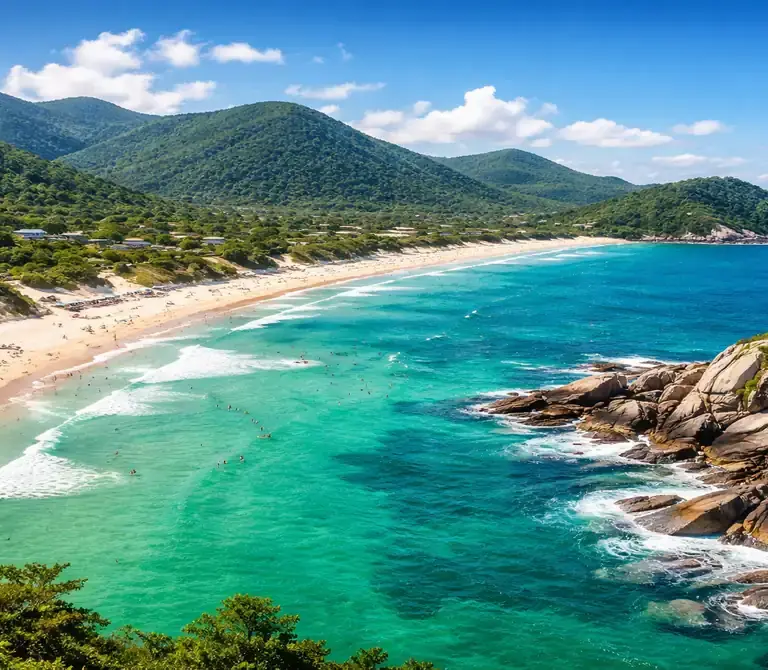 Paisagem aérea de uma praia paradisíaca no Sul do Brasil, com mar verde-esmeralda, areia branca e vegetação nativa, representando o litoral de Santa Catarina.