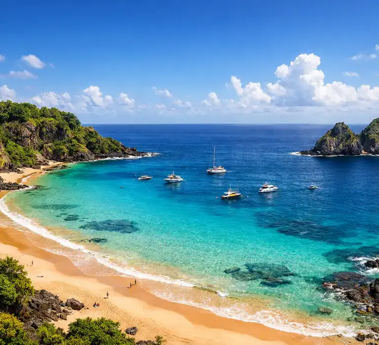 Vista panorâmica da Baía do Sancho em Fernando de Noronha, com mar azul-turquesa e falésias verdes.