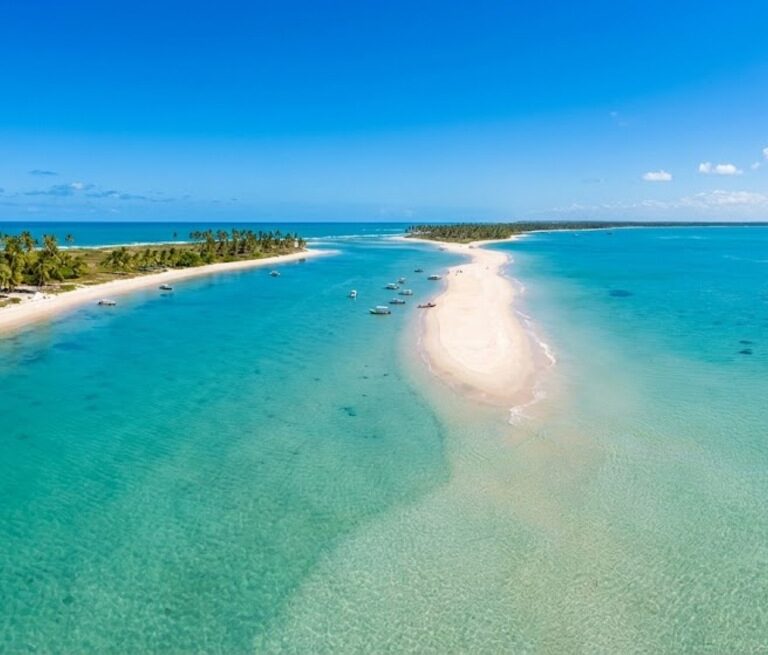 Vista aérea da Ponta do Corumbau, na Bahia, com sua faixa de areia entrando no mar azul-turquesa.