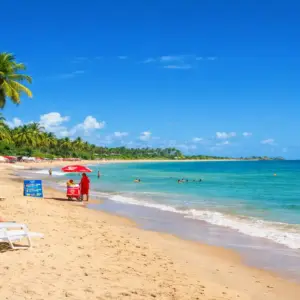 "Paisagem panorâmica da Praia de Taperapuã em Porto Seguro com céu azul vibrante e mar calmo, ilustrando a melhor época para viajar para a Bahia sem chuvas."