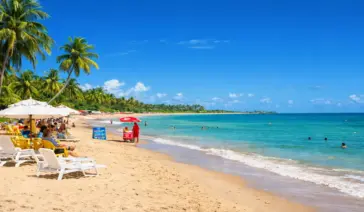 "Paisagem panorâmica da Praia de Taperapuã em Porto Seguro com céu azul vibrante e mar calmo, ilustrando a melhor época para viajar para a Bahia sem chuvas."