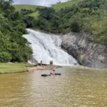 Vista panorâmica da Cachoeira Rio do Meio em Santa Leopoldina, mostrando a ampla queda d'água rochosa e a área de banho com banhistas aproveitando a piscina natural
