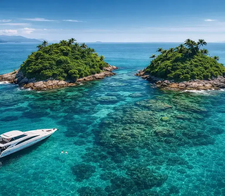 Vista aérea da Ilha Duas Irmãs em Angra dos Reis, com suas duas formações rochosas cercadas por mar azul-turquesa e uma lancha privativa ancorada.