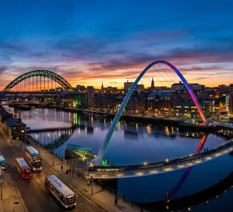 Vista panorâmica das pontes iluminadas sobre o Rio Tyne em Newcastle, Inglaterra, ao anoitecer.