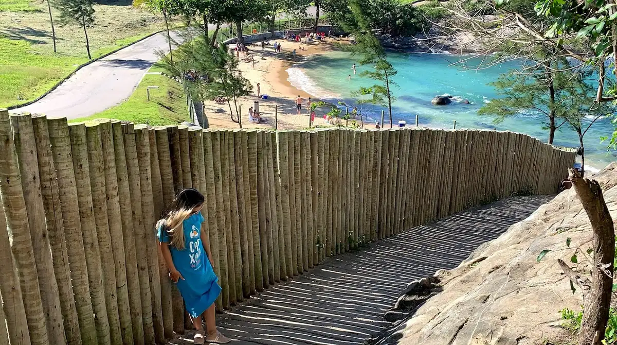 Por que todo mundo ama esses 8 lugares no Espírito Santo? 9 Mulher observando o mar turquesa em uma praia tranquila do Espírito Santo, com acesso por uma escadaria de madeira rústica.
