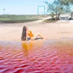Turista boiando de costas sem esforço na água de tom rosado da Lagoa Vermelha, em Arraial do Cabo.