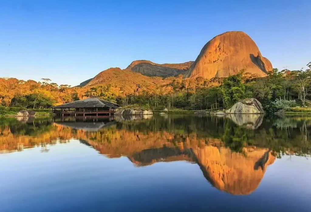 A famosa Pedra Azul refletida no lago durante o pôr do sol em Domingos Martins, cenário das melhores pousadas da região.