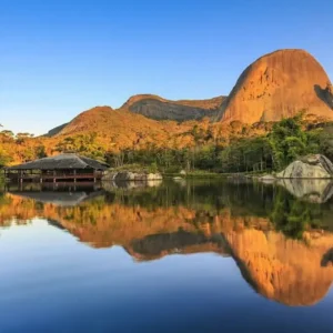 A famosa Pedra Azul refletida no lago durante o pôr do sol em Domingos Martins, cenário das melhores pousadas da região.
