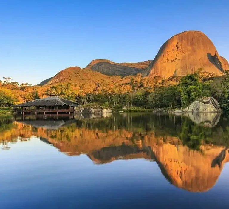A famosa Pedra Azul refletida no lago durante o pôr do sol em Domingos Martins, cenário das melhores pousadas da região.
