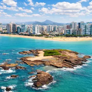 Vista panorâmica da Ilha Pituã em Vila Velha, com suas águas cristalinas e barcos de pescadores ancorados próximos às piscinas naturais, com a Praia de Itapuã ao fundo.