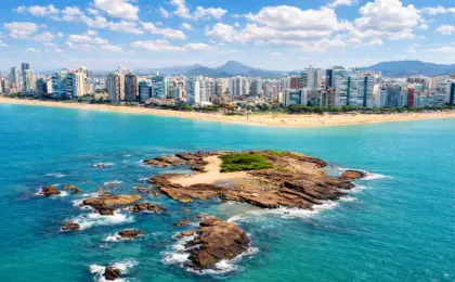 O 'Caribe' fica em Vila Velha: Como chegar às piscinas naturais da Ilha Pituã 10 Vista panorâmica da Ilha Pituã em Vila Velha, com suas águas cristalinas e barcos de pescadores ancorados próximos às piscinas naturais, com a Praia de Itapuã ao fundo.