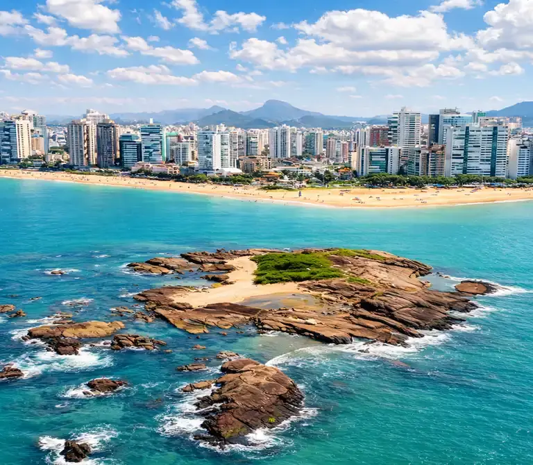 Vista panorâmica da Ilha Pituã em Vila Velha, com suas águas cristalinas e barcos de pescadores ancorados próximos às piscinas naturais, com a Praia de Itapuã ao fundo.