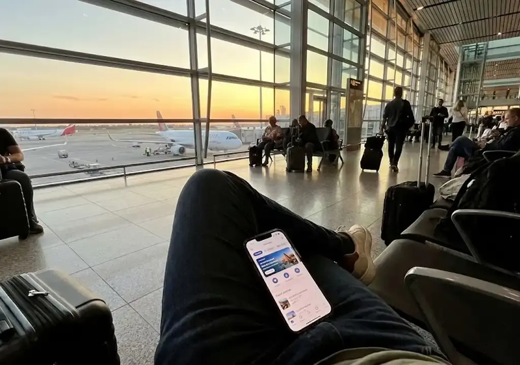 Viajante usando aplicativo de celular para buscar passagens aéreas baratas em um aeroporto.