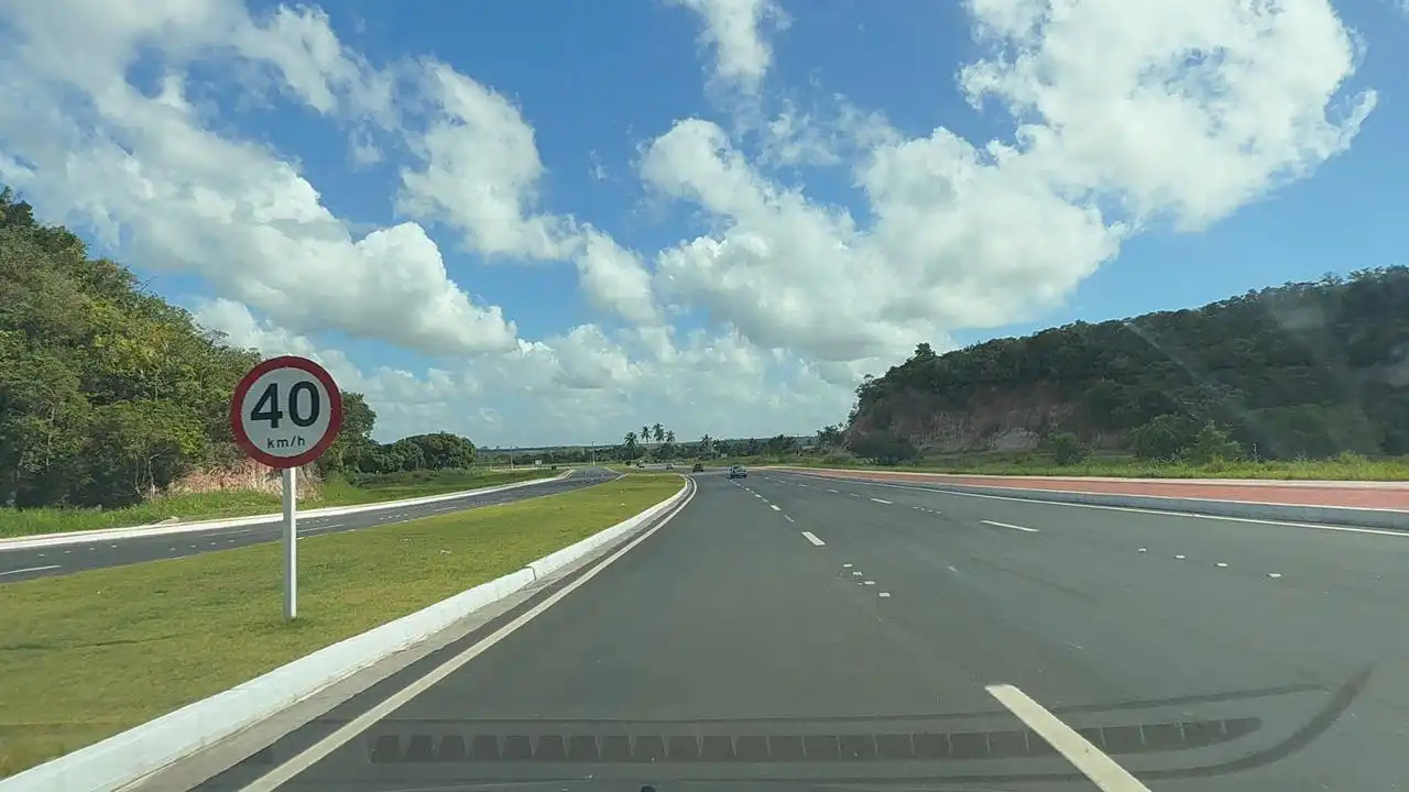 "Vista da nova Rodovia ES-115, o Contorno de Jacaraípe, na Serra, Espírito Santo. A imagem mostra pistas duplas asfaltadas, sinalização moderna e fluxo livre de veículos em dia de sol."