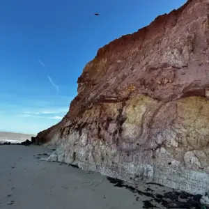 Vista impressionante dos paredões de falésias avermelhadas na orla de Marataízes, Espírito Santo, com piscinas naturais de águas calmas formadas na areia durante a maré baixa.