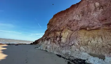 Vista impressionante dos paredões de falésias avermelhadas na orla de Marataízes, Espírito Santo, com piscinas naturais de águas calmas formadas na areia durante a maré baixa.