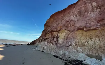 Falésias em Marataízes: Um Cenário Surpreendente no Litoral Capixaba 11 Vista impressionante dos paredões de falésias avermelhadas na orla de Marataízes, Espírito Santo, com piscinas naturais de águas calmas formadas na areia durante a maré baixa.