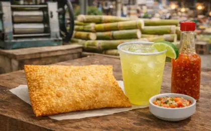 Rota do Pastel no Espírito Santo: 5 Lugares para Comer 10 Close apetitoso de um pastel de feira frito e dourado, com massa crocante, ao lado de um copo de inox suado com caldo de cana gelado e limão. Representação da baixa gastronomia capixaba.