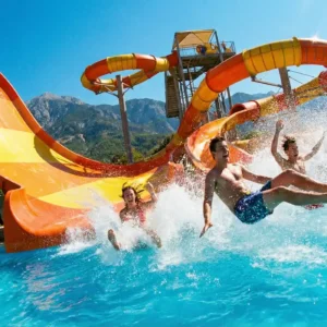 Jovens descendo em alta velocidade por um toboágua laranja e caindo na piscina, com muita água espirrando, ilustrando a diversão nos parques aquáticos