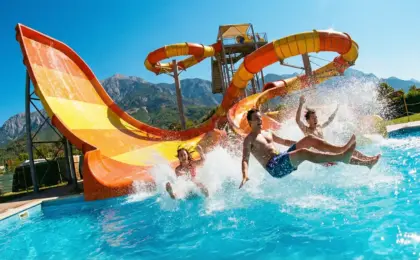 Jovens descendo em alta velocidade por um toboágua laranja e caindo na piscina, com muita água espirrando, ilustrando a diversão nos parques aquáticos