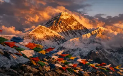 Monte Everest: O Lado Sombrio da "Zona da Morte 8 Pico do Monte Everest com nuvens dramáticas e bandeiras de oração, ilustrando o ambiente hostil da Zona da Morte.