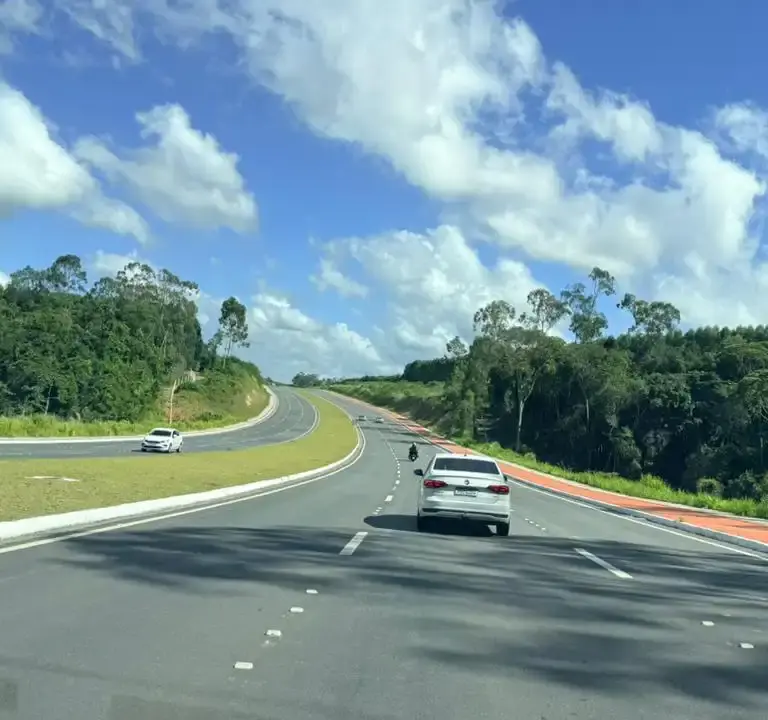 Vista da nova Rodovia ES-115, o Contorno de Jacaraípe, na Serra, Espírito Santo. A imagem mostra pistas duplas asfaltadas, sinalização moderna e fluxo livre de veículos em dia de sol.