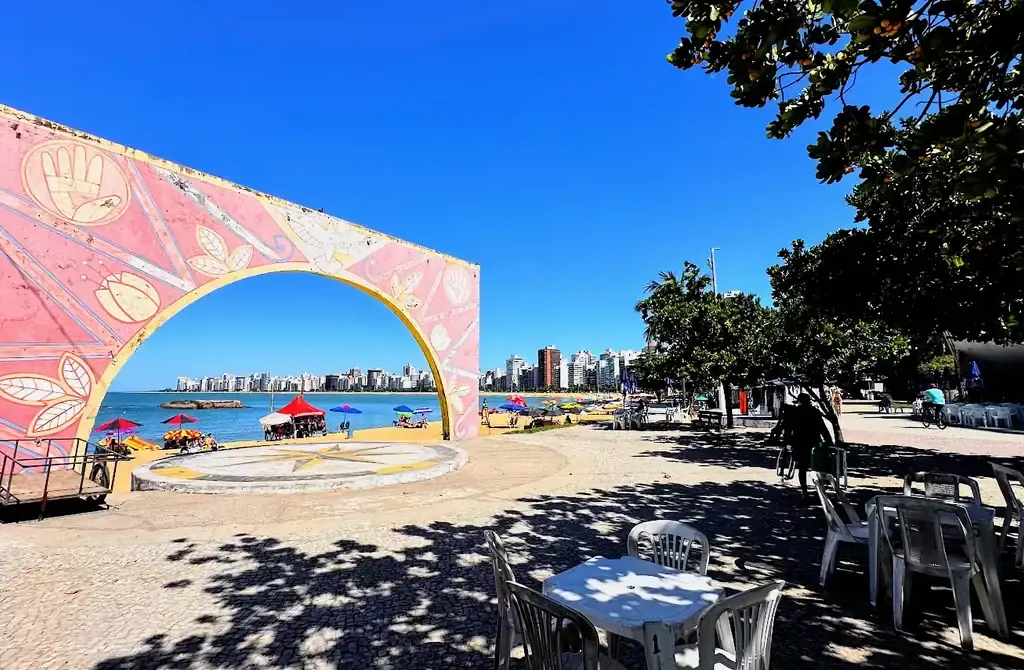Vista aérea da Arena de Verão na Praia da Costa, Vila Velha, com quadras de esporte lotadas, palco de shows e área gastronômica na areia.