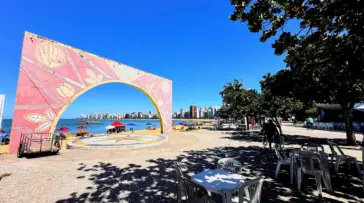 Vista aérea da Arena de Verão na Praia da Costa, Vila Velha, com quadras de esporte lotadas, palco de shows e área gastronômica na areia.