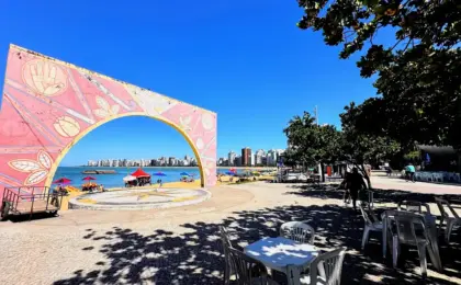 Vista aérea da Arena de Verão na Praia da Costa, Vila Velha, com quadras de esporte lotadas, palco de shows e área gastronômica na areia.