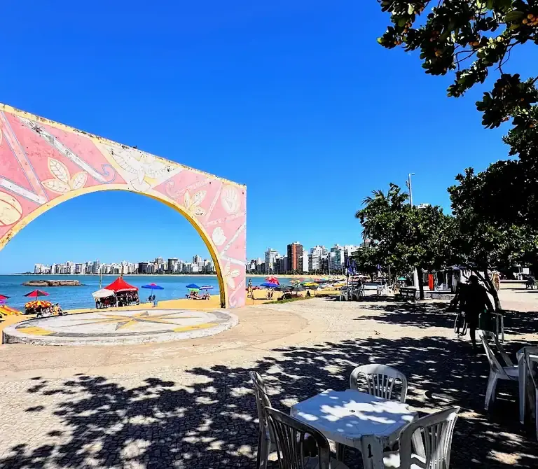 Vista aérea da Arena de Verão na Praia da Costa, Vila Velha, com quadras de esporte lotadas, palco de shows e área gastronômica na areia.