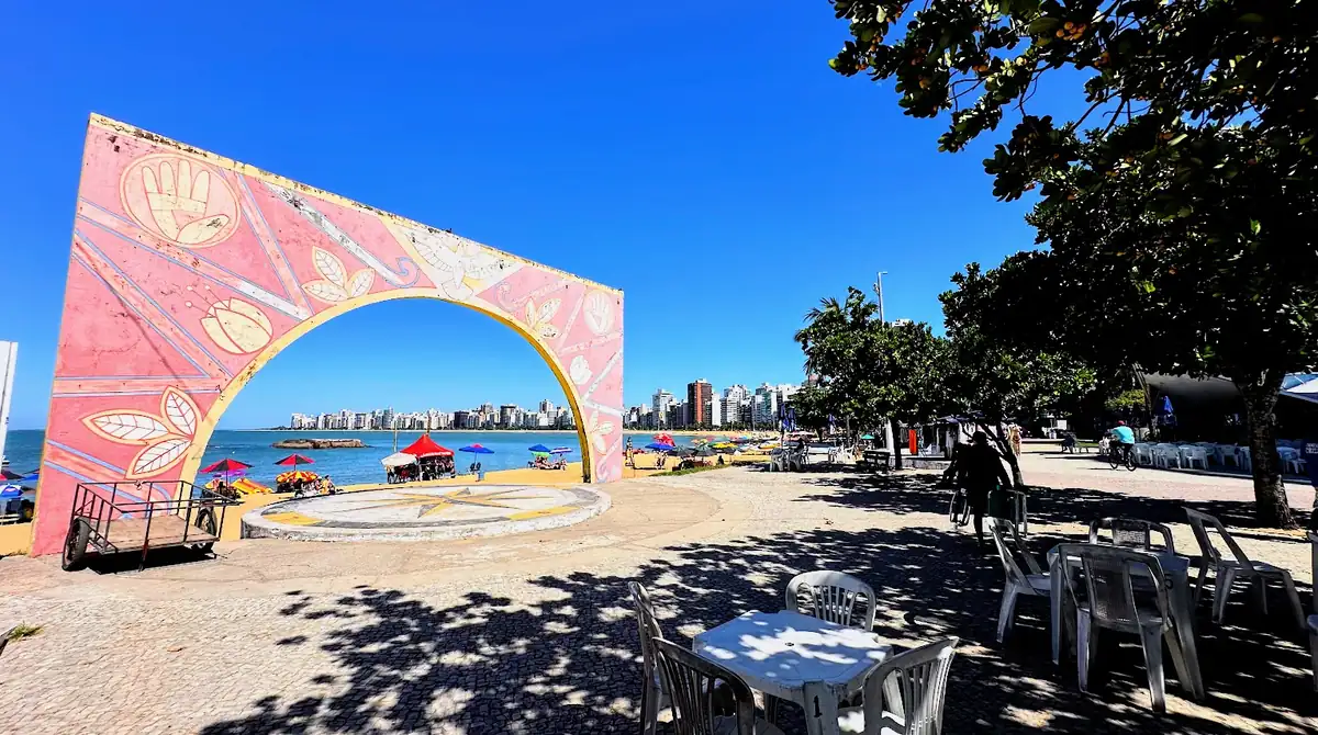 Vista aérea da Arena de Verão na Praia da Costa, Vila Velha, com quadras de esporte lotadas, palco de shows e área gastronômica na areia.