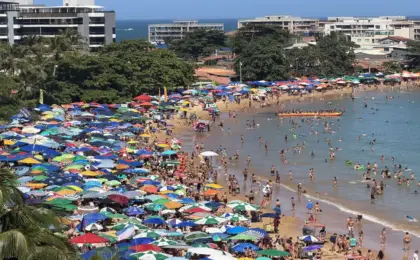 Peracanga lotada! Enseada Azul ferve com milhares de turistas nesta sexta. 12 Vista panorâmica da Praia de Peracanga, em Guarapari, completamente lotada. A faixa de areia está coberta por centenas de guarda-sóis coloridos e muitos banhistas aproveitam o mar calmo da Enseada Azul em um dia de sol.