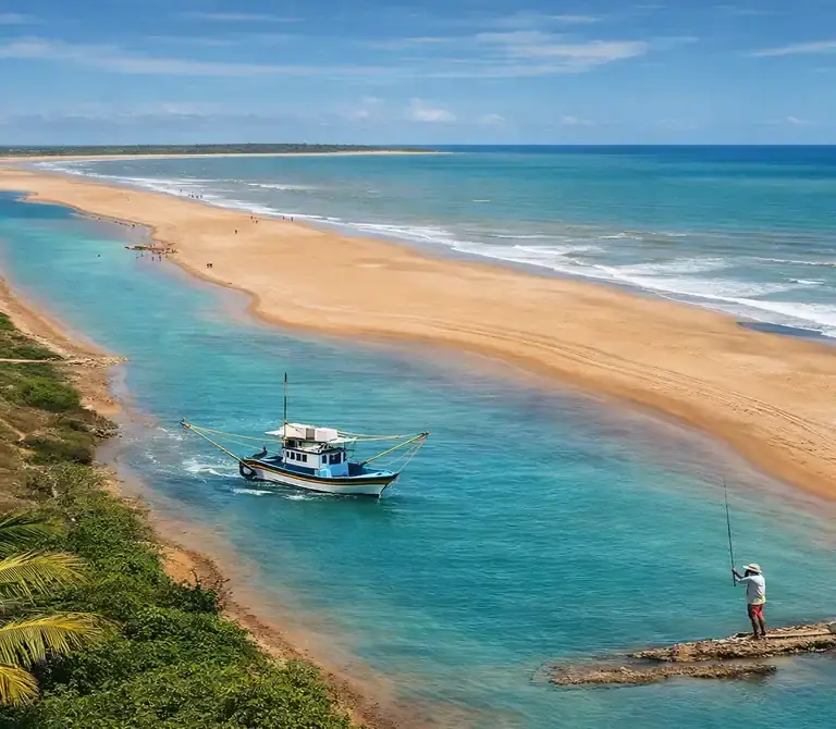 Vista aérea ensolarada da Praia de Urussuquara, no Espírito Santo, mostrando o rio de águas turquesas correndo paralelo ao mar, com um barco de pesca e vegetação nativa.