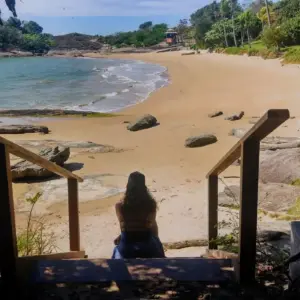 Vista da Praia dos Ventos em Guarapari, com mar calmo e transparente e pedras na lateral.