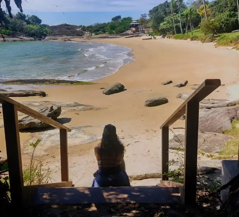 Vista da Praia dos Ventos em Guarapari, com mar calmo e transparente e pedras na lateral.