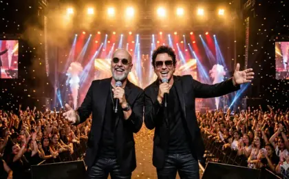 Dupla sertaneja Rick e Renner sorrindo e cantando com microfones no palco, com chuva de papel picado e público ao fundo.