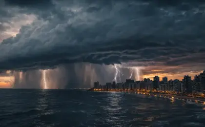 Virada no Tempo: Frente fria e ZCAS trazem chuvas de até 400mm para o Sudeste 7 Tempestade dramática com múltiplos raios caindo no mar próximo à linha do horizonte de uma cidade costeira durante o crepúsculo. Cortinas de chuva intensa são visíveis sob uma nuvem escura e massiva.